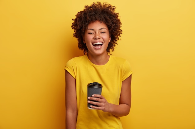 Mulher jovem com corte de cabelo afro e camiseta amarela segurando uma xícara de café