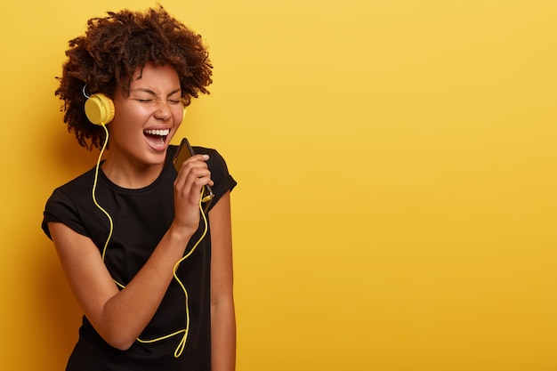 Mulher jovem com corte de cabelo afro e fones de ouvido amarelos