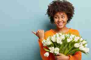 Foto grátis mulher jovem com corte de cabelo afro segurando um buquê de flores brancas