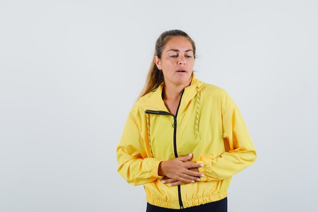 Mulher jovem com dor de barriga, vestindo uma capa de chuva amarela e parecendo preocupada