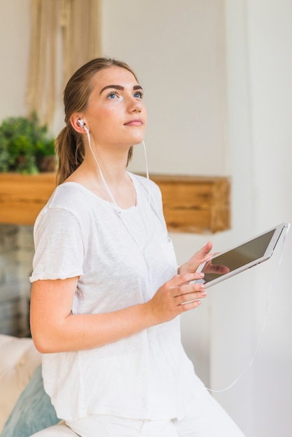 Mulher jovem, com, fone ouvido, segurando, tablete digital, olhando