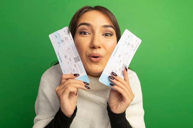 Mulher jovem com lenço branco segurando passagens aéreas e sorrindo