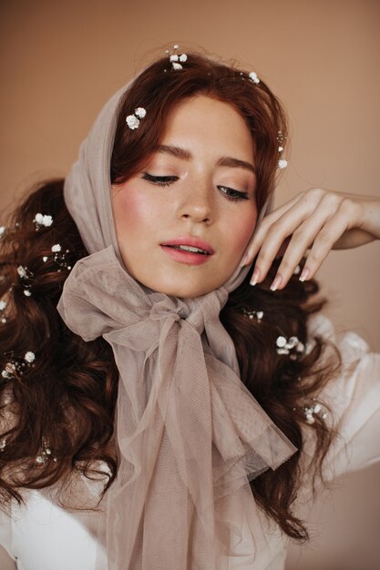 Mulher jovem com lenço transparente na cabeça toca suavemente seu rosto e olha para baixo com modéstia.