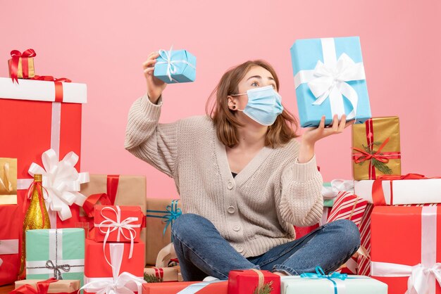 Mulher jovem com máscara sentada de frente em um presente de Natal