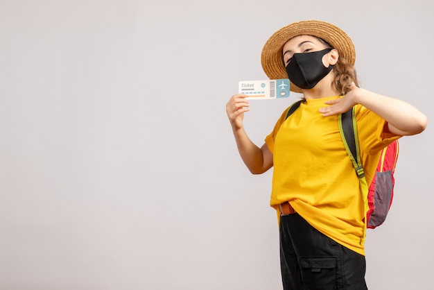 Mulher jovem com mochila e máscara preta segurando um bilhete de viagem