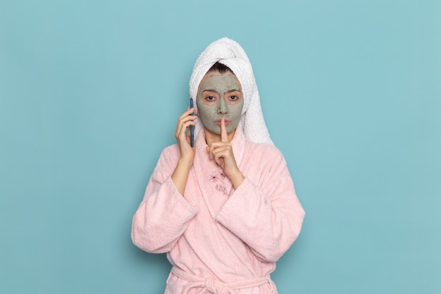 Mulher jovem com roupão rosa após o banho falando ao telefone na parede azul beleza água limpa autocuidado creme chuveiro