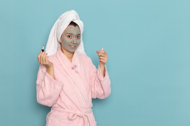 Mulher jovem com roupão rosa após o banho segurando esmalte na parede azul beleza água limpa chuveiro