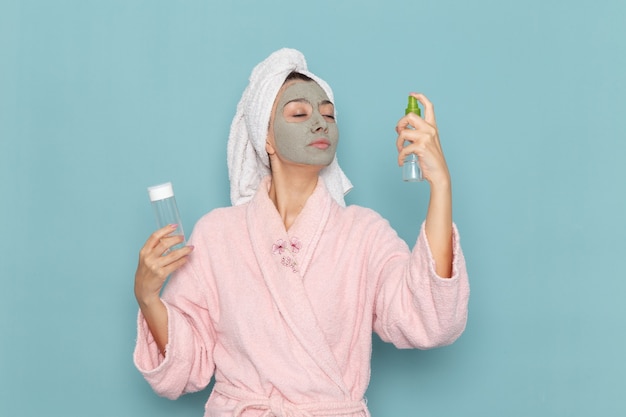 Mulher jovem com roupão rosa após o banho segurando sprays na parede azul beleza banho de água creme banho de chuveiro