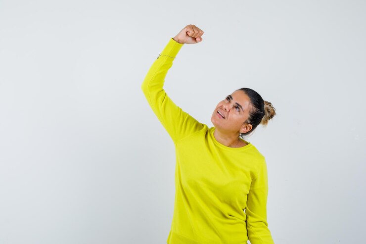 Foto grátis mulher jovem com suéter amarelo e calça preta cerrando os punhos e parecendo feliz