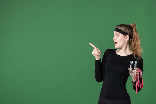 Mulher jovem com um copo de água e medida da cintura no fundo verde cor de fundo verde saúde corpo treino mulher atleta de vista frontal