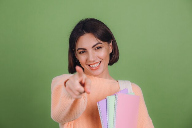 Mulher jovem com um suéter casual cor de pêssego e uma mochila isolada na parede verde oliva