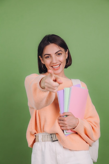 Mulher jovem com um suéter casual cor de pêssego e uma mochila isolada na parede verde oliva