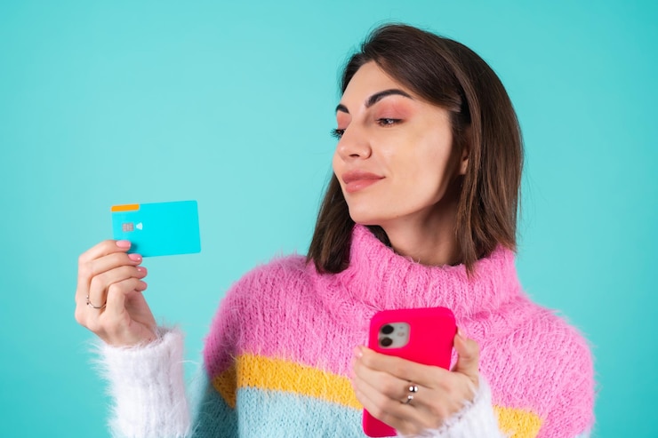 Foto grátis mulher jovem com um suéter multicolorido brilhante azul segurando um cartão de crédito