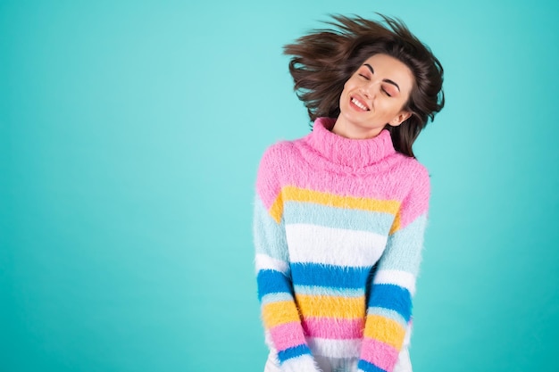 Mulher jovem com um suéter multicolorido brilhante em azul sorrindo fofo com os olhos fechados