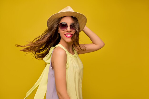 Mulher jovem com um vestido amarelo com chapéu e óculos de sol