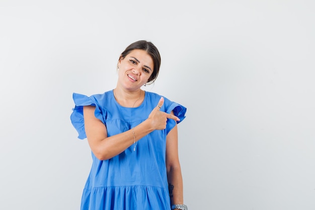 Mulher jovem com um vestido azul apontando para o lado e parecendo otimista