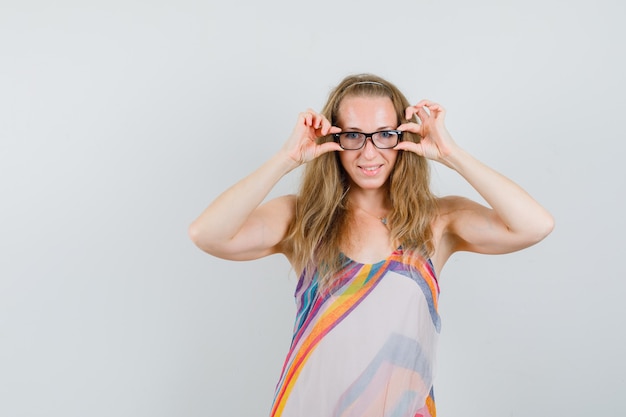 Foto grátis mulher jovem com um vestido de verão, mantendo os dedos nos óculos e parecendo alegre