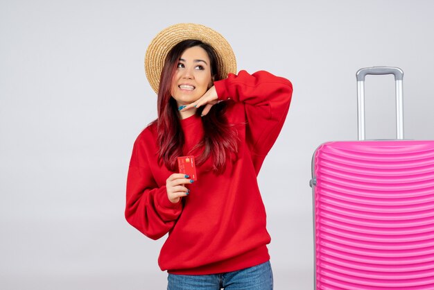 Mulher jovem com uma bolsa rosa segurando o cartão do banco na parede branca de frente