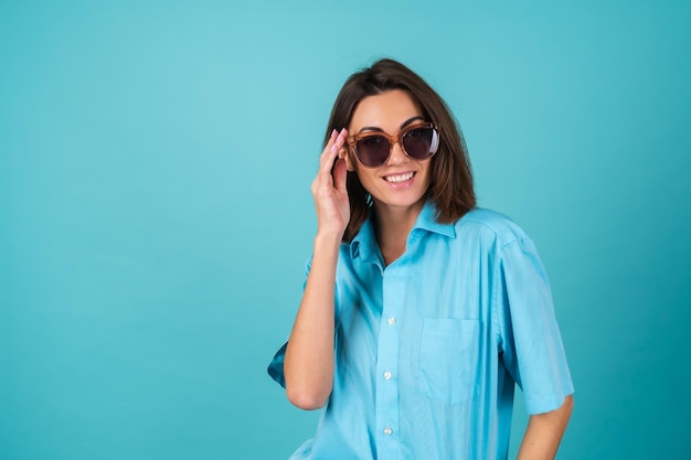 Mulher jovem com uma camisa azul em uma parede com óculos de sol, posando com estilo elegante