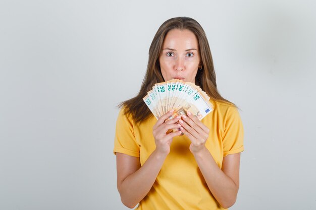 Mulher jovem com uma camiseta amarela, segurando notas de euro e olhando com cuidado