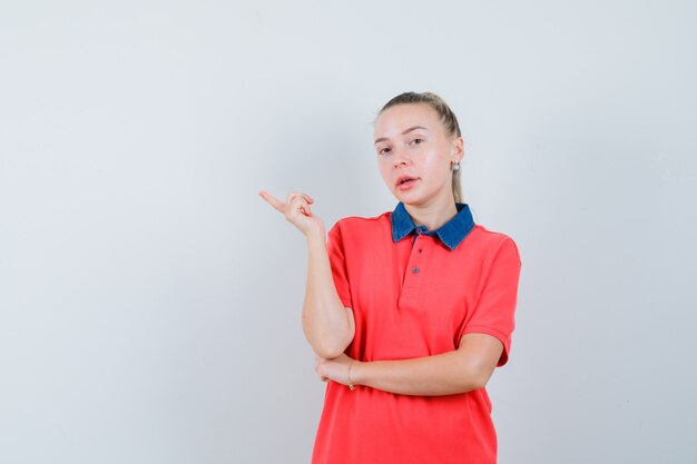 Mulher jovem com uma camiseta apontando para o lado e parecendo confiante