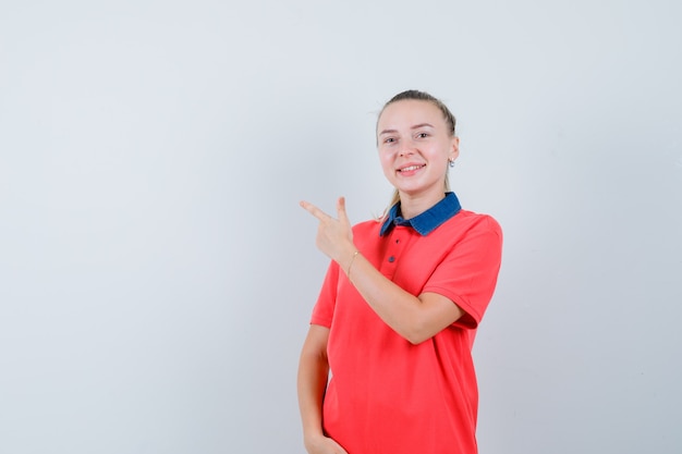 Mulher jovem com uma camiseta apontando para o lado esquerdo superior e parecendo feliz