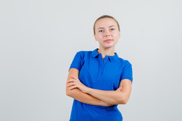 Mulher jovem com uma camiseta azul em pé com os braços cruzados e parecendo confiante