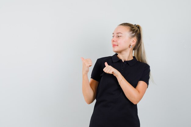 Mulher jovem com uma camiseta preta apontando para o lado esquerdo superior, sorrindo e parecendo otimista