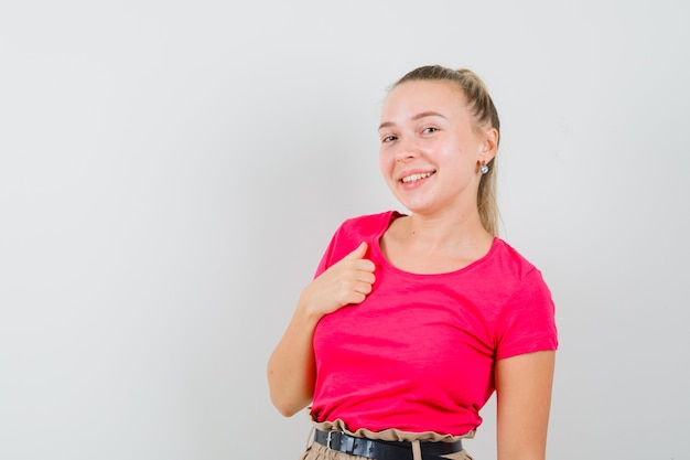 Foto grátis mulher jovem com uma camiseta rosa posando com a mão no peito e parecendo alegre