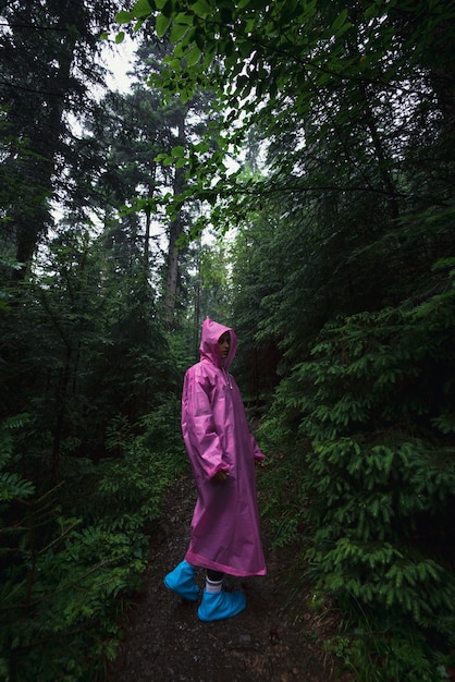 Mulher jovem com uma capa de chuva caminhando pela floresta na chuva