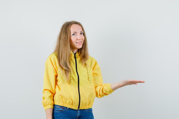 Mulher jovem com uma jaqueta amarela e jeans azul, levantando a mão e segurando algo imaginário