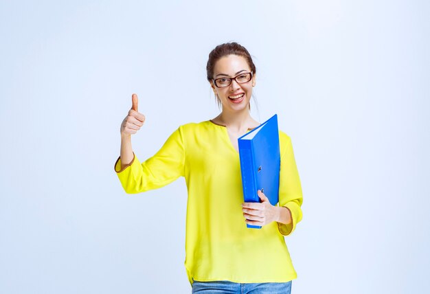 Mulher jovem com uma pasta azul mostrando um sinal de satisfação