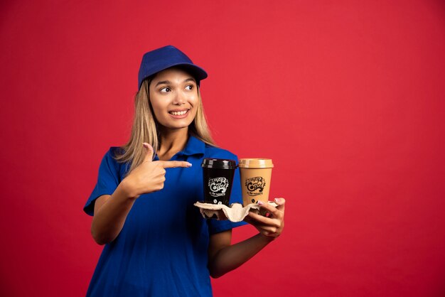 Mulher jovem com uniforme azul, apontando para uma caixa com duas xícaras.