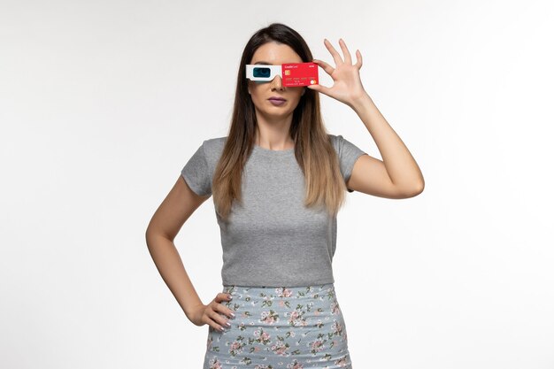 Mulher jovem com vista frontal segurando o cartão do banco vermelho em óculos de sol d na superfície branca