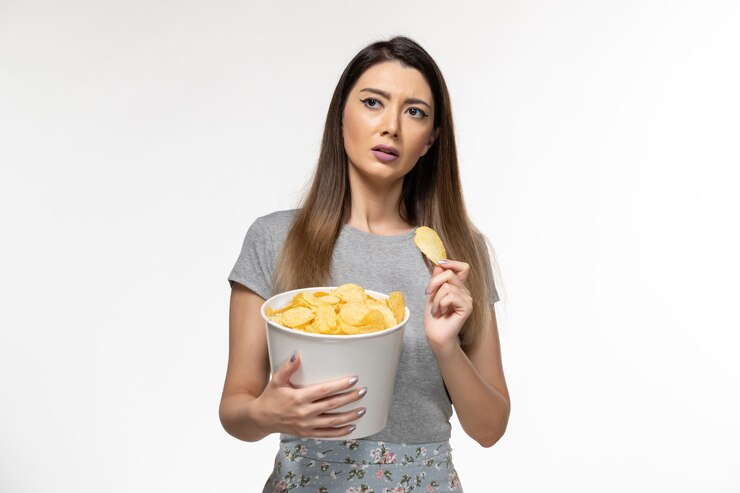 Foto grátis mulher jovem comendo cips e assistindo filme na superfície branca de frente