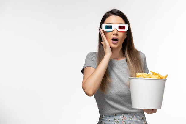 Foto grátis mulher jovem comendo cips enquanto assiste filme com óculos de sol na superfície branca