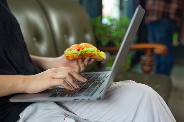 Mulher jovem comendo sanduíches de croissant na sala do escritório