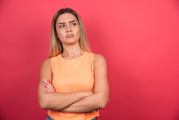 Mulher jovem confusa com os braços cruzados, olhando para os lados.