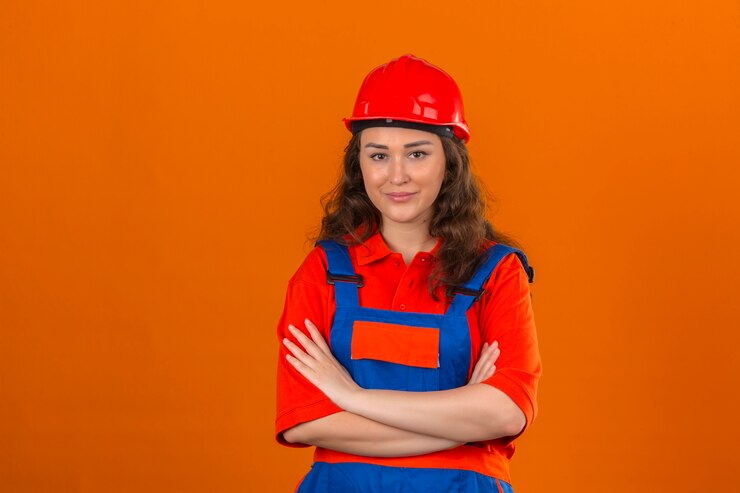 Foto grátis mulher jovem construtor em uniforme de construção e capacete de segurança em pé com os braços cruzados com sorriso no rosto sobre parede laranja isolada
