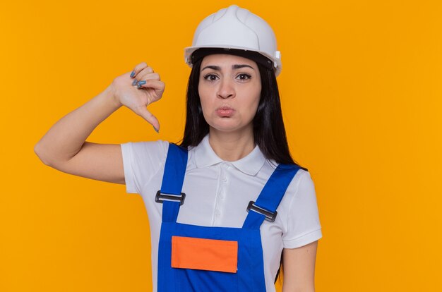 Mulher jovem construtora com uniforme de construção e capacete de segurança, olhando para a câmera