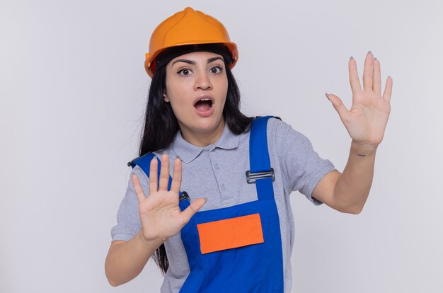 Mulher jovem construtora com uniforme de construção e capacete de segurança parecendo preocupada