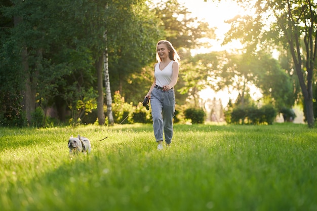 Mulher jovem correndo com bulldog francês no parque