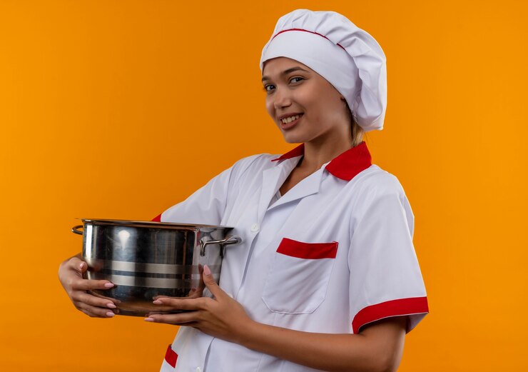 Foto grátis mulher jovem cozinheira sorridente usando uniforme de chef segurando uma panela sobre fundo laranja isolado