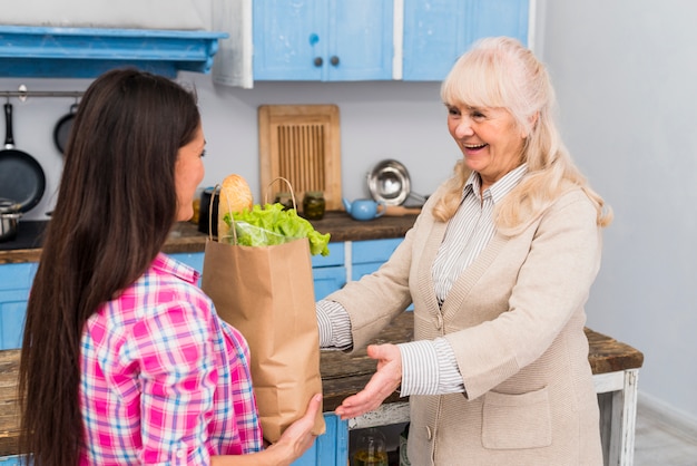 Mulher jovem, dar, sacola mantimentos, para, dela, mãe sênior, cozinha