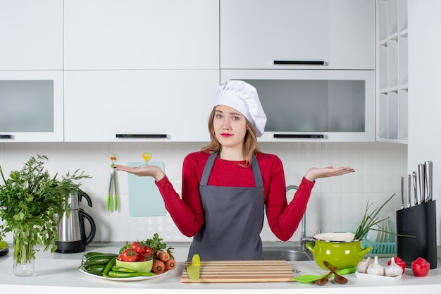 Foto grátis mulher jovem de avental em pé atrás da mesa perplexa vista frontal