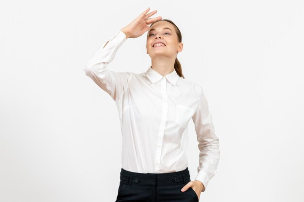 Mulher jovem de blusa branca olhando para longe no fundo branco.