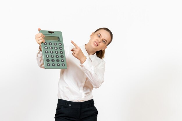 Mulher jovem de blusa branca segurando uma calculadora enorme na mesa branca.