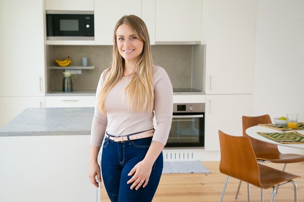 Mulher jovem de cabelos louros feliz posando na cozinha