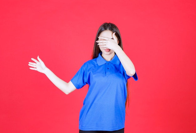 Mulher jovem de camisa azul em pé na parede vermelha e apontando para alguém ao redor