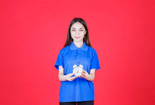 Mulher jovem de camisa azul segurando um despertador